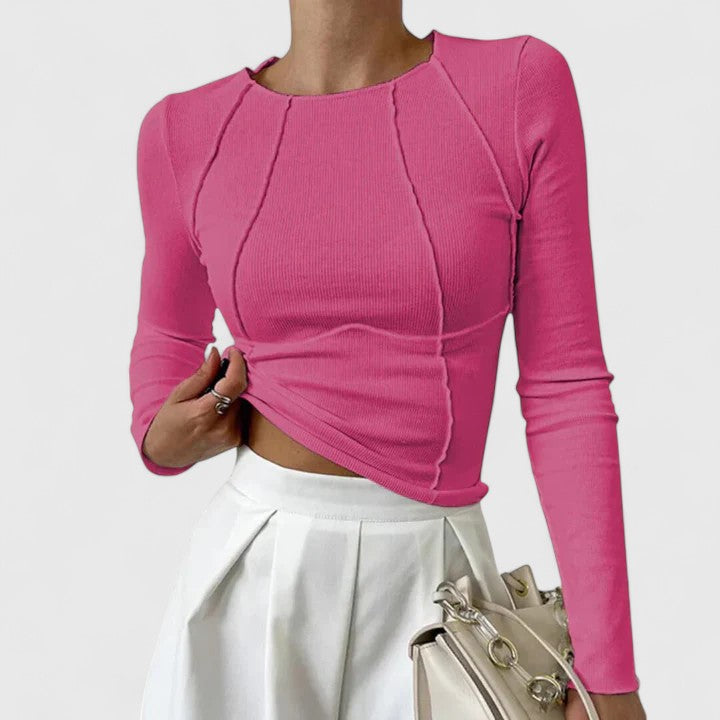 Pink long-sleeve knit top with cropped asymmetric hem and twisted front seams.