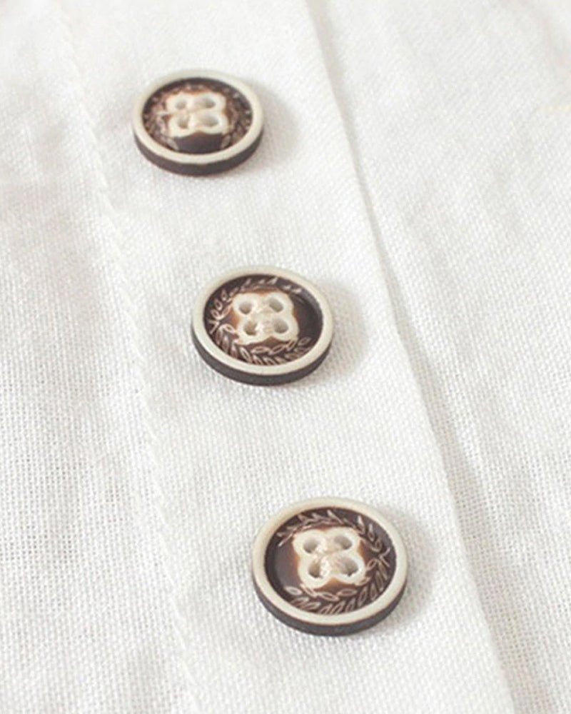 Close-up of three round dark buttons on a white fabric placket