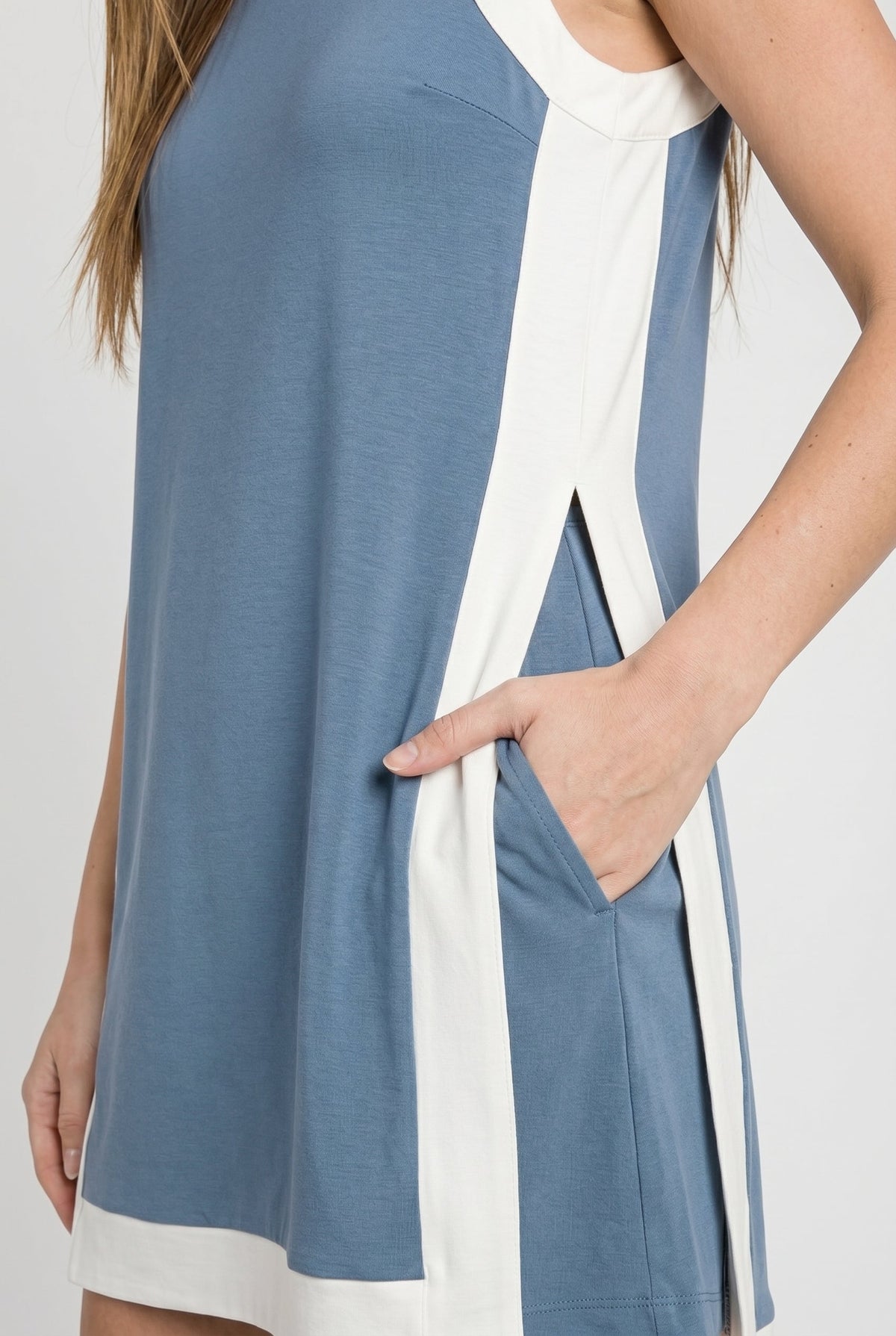 Blue tunic dress detail with white side panels, pocket opening, and curved hem trim